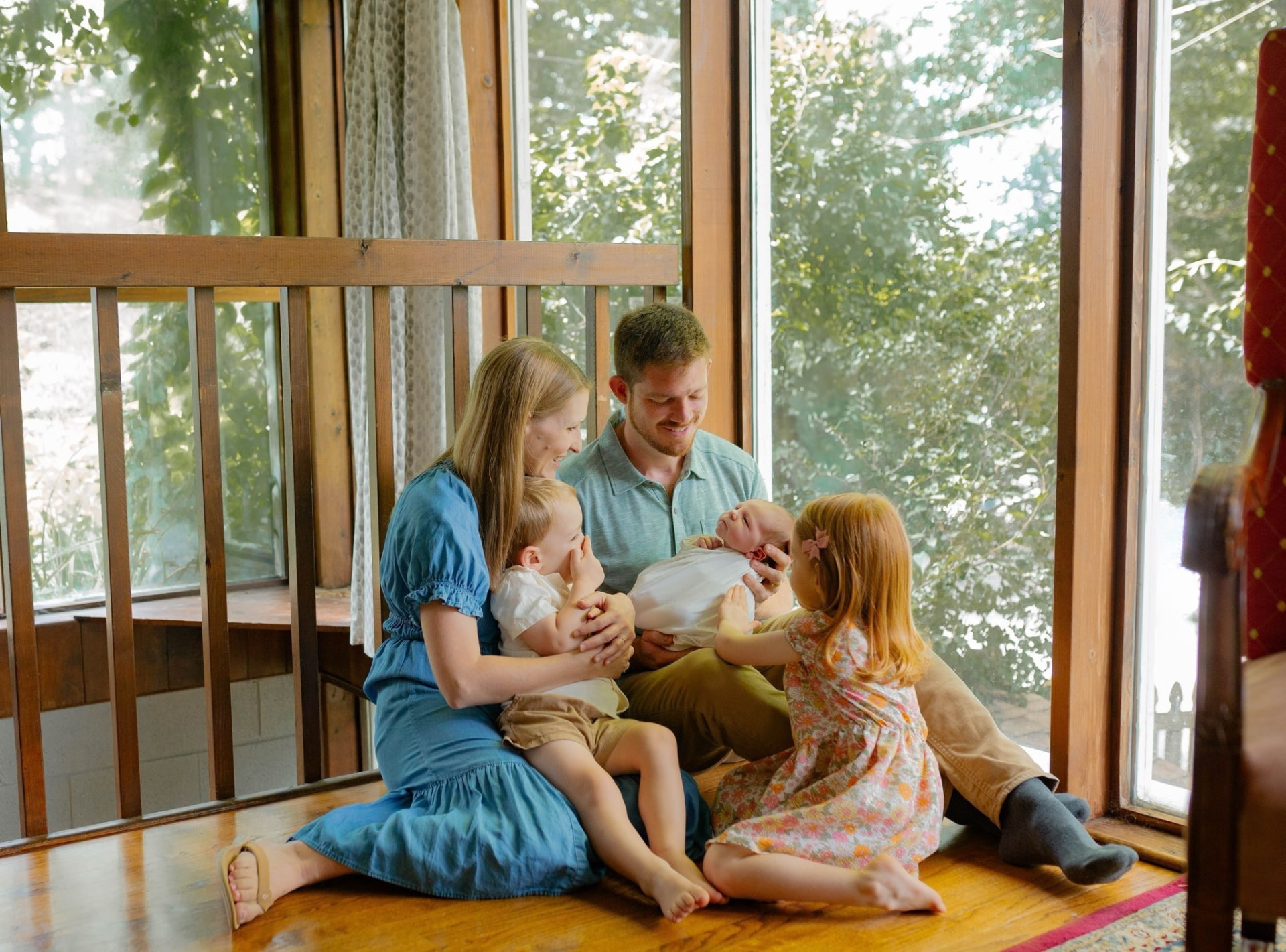 Jake Keller with his wife and three children sitting together in a sunlit room with green foliage visible through the windows.